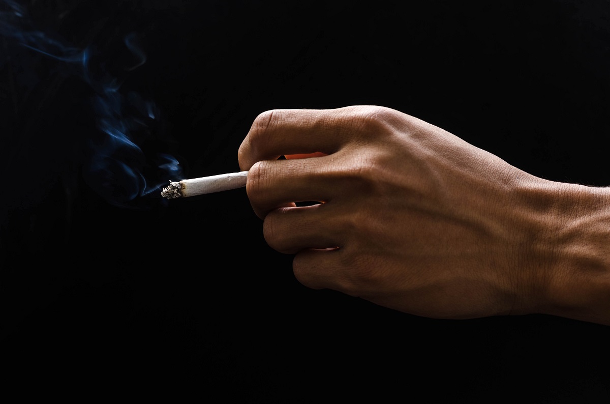 hand holding cigarette and smoke on black